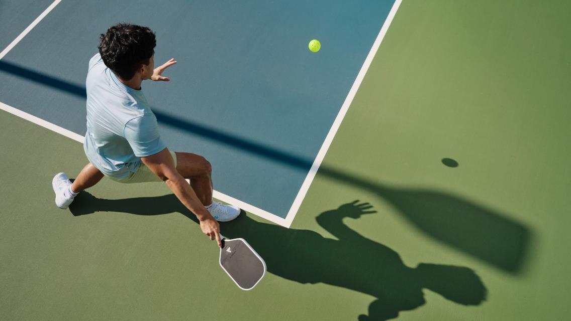 A pickleball player lunging for a shot on a sunlit outdoor court